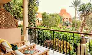 Ulkotila, jossa on huonekaluja, edessä rehevä puutarha ja kupolikattoinen rakennus. (Tekoälyn luoma teksti)