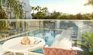 Näkymä terassilta, jossa näkyy uima-allas, aurinkovuoteita ja aurinkovarjoja vehreyden ympäröimänä. (Tekoälyn luoma teksti)