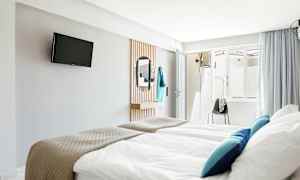 Hotellihuone, jossa vuoteet, TV seinällä ja peili. (Tekoälyn luoma teksti)