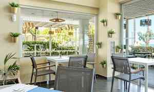 Modernisti sisustettu kahvila, jossa on pöytiä ja tuoleja; näkymä vehreisiin puihin ja ulkokalusteisiin. (Tekoälyn luoma teksti)