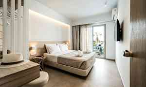 Hotellihuone, jossa on parisänky, televisio ja parvekeovi. Kirjoituspöytä, jossa hattu ja tuoli. (Tekoälyn luoma teksti)