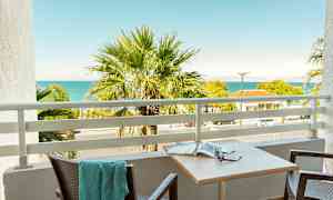 Parveke, josta näkyy palmu, meri ja naapurirakennuksia. (Tekoälyn luoma teksti)