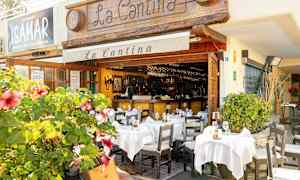 Ravintola ulkotarjoilualueella, koristeltu valkoisilla pöytäliinoilla ja kukkivilla kasveilla. (Tekoälyn luoma teksti)