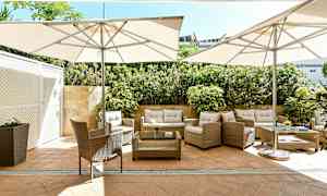 Ulkokalusteet varjojen alla kiviterassilla, jota ympäröivät kasvit. (Tekoälyn luoma teksti)