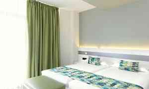 Hotellihuone, jossa kaksi erillisvuodetta, vihreät verhot ja yhteensopivat sängyn koristeet. (Tekoälyn luoma teksti)