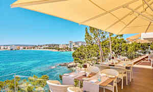 Ulkoterassi, josta on näkymä kirkkaansiniseen lahtimereen ja taustalla oleviin rakennuksiin. (Tekoälyn luoma teksti)