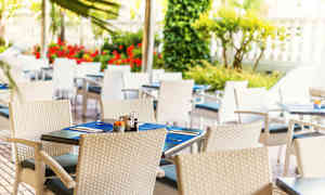 Ulkoterassi valkoisilla punotuilla tuoleilla ja sinisin pöytätabletein katetuilla pöydillä. (Tekoälyn luoma teksti)