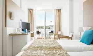 Moderni hotellihuone, jossa vuoteet, televisio ja istuimet, sekä parveke näkymillä. (Tekoälyn luoma teksti)