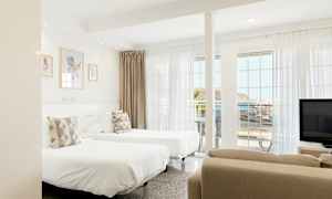 Valoisa hotellihuone, jossa on kaksi erillistä vuodetta, suuret ikkunat ja merinäköala. (Tekoälyn luoma teksti)