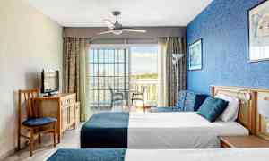 Hotellihuoneen kuva, jossa on kaksi vuodetta, sininen seinä ja lasiovi parvekkeelle. (Tekoälyn luoma teksti)