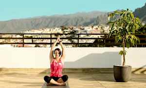 Henkilö istuu jooga-asennossa terassilla näkymä kaupunkiin ja vuorille. (Tekoälyn luoma teksti)