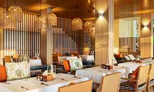 Ravintola, jossa on katettuja pöytiä ja roikkuvia punottuja lampunvarjostimia. (Tekoälyn luoma teksti)