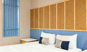 Makuuhuone, jossa sänky, tyynyjä ja sininen seinä, jossa punottuja paneeleja. (Tekoälyn luoma teksti)