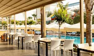 Ulkoilmaravintola uima-altaan lähellä, taustalla aurinkovarjoja ja aurinkotuoleja. (Tekoälyn luoma teksti)