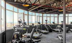 Valoisa kuntosali kuntosalilaitteilla ja näköala suurten ikkunoiden läpi. (Tekoälyn luoma teksti)