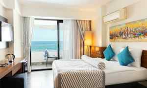 Hotellihuone, jossa on iso sänky, siniset tyynyt ja merinäköala parvekkeelta. (Tekoälyn luoma teksti)