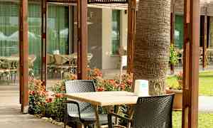 Ulkoalue, jossa pöytiä, tuoleja ja kukkia rakennuksen lasi-ikkunoiden edessä. (Tekoälyn luoma teksti)