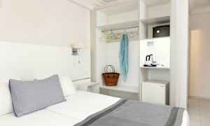 Hotellihuone, jossa sänky, vaatekaappi ja pieni jääkaappi. (Tekoälyn luoma teksti)