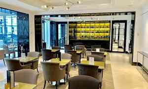 Moderni kahvila, jossa tyylikkäät pöydät ja tuolit sekä hyvin varusteltu taustapeili takana. (Tekoälyn luoma teksti)