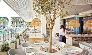 Ravintola, josta on näkymä uima-altaalle ja moderneihin huoneistoihin, sisältää oliivipuukoristeen ja rottinkivalaisimet. (Tekoälyn luoma teksti)