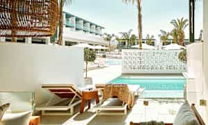 Aurinkotuoleja uima-altaan äärellä, taustalla modernia arkkitehtuuria. (Tekoälyn luoma teksti)