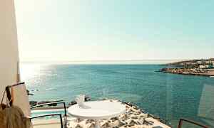 Parveke merinäköalalla, aurinkovarjoja uima-altaalla ja kuppi pöydällä. (Tekoälyn luoma teksti)