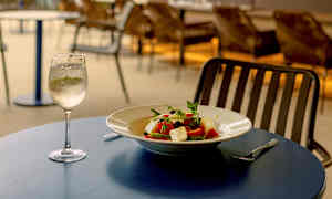 Ravintolan ulkoterassi meren rannalla, pöydällä salaattiannos ja lasillinen valkoviiniä. (Tekoälyn luoma teksti)