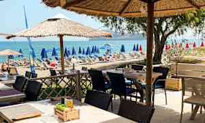 Ulkoterassi, jossa on varjot, lähellä rantaa aurinkotuoleineen ja näkymä merelle. (Tekoälyn luoma teksti)