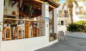 Ulkobaari, jossa puiset tuolit ja tiilikatto. Taustalla näkyy palmu ja rakennuksia. (Tekoälyn luoma teksti)