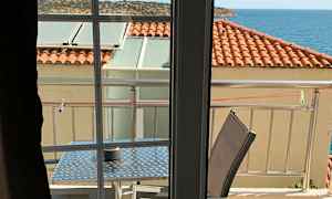 Näkymä huoneesta parvekkeelle, jossa on pöytä ja tuolit, katto punaisilla kattotiilillä ja taustalla meri. (Tekoälyn luoma teksti)