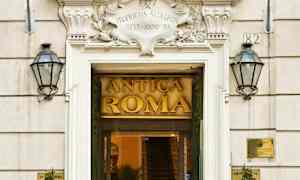 Sisäänkäynti rakennukseen, jossa kyltti Antica Roma, ympäröitynä kahdella lipulla ja kasvikoristeilla. (Tekoälyn luoma teksti)