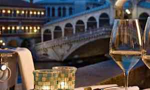 Vadillinen äyriäisiä ja lasillinen valkoviiniä pöydällä, josta on näkymä valaistulle sillalle iltahämärässä. (Tekoälyn luoma teksti)