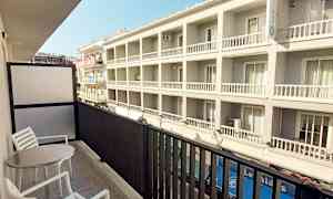 Parveke, jossa on kaksi tuolia ja pöytä, näkymä moderniin rakennukseen. (Tekoälyn luoma teksti)