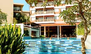 Uima-allas, jossa kirkasta sinistä vettä, ympäröitynä kasveilla sekä hotelli taustalla. (Tekoälyn luoma teksti)