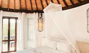 Makuuhuoneen sisustus, jossa on punotusta puusta valmistettu katto, valkoinen sänky hyttysverkon kanssa ja ikkunat, joista tulvii luonnonvaloa. (Tekoälyn luoma teksti)