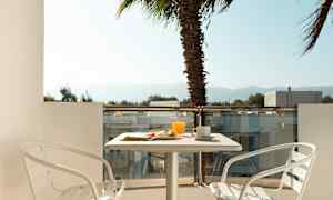 Parveke, jossa pöytä, kaksi valkoista tuolia ja tarjoiltu aamiainen. Taustalla näkyy palmu. (Tekoälyn luoma teksti)