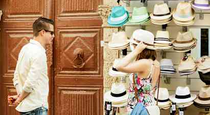 Henkilö kokeilee hattua myyntipöydän ääressä, jossa on erilaisia hattuja. (Tekoälyn luoma teksti)