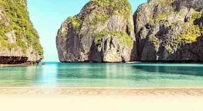 Hiekkaranta, joka avautuu rauhalliseen, siniseen veteen, ympäröitynä korkeilla kasvillisuuden peittämillä kallioilla. (Tekoälyn luoma teksti)