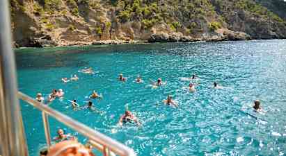 Ihmisiä uimassa kirkkaassa sinisessä vedessä kallioisen rannikon edustalla. (Tekoälyn luoma teksti)