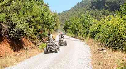 Ihmiset ajavat mönkijöillä soratietä, jota ympäröi vehreys. (Tekoälyn luoma teksti)