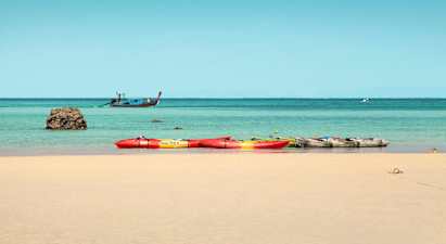 Useita kajakkeja hiekkarannalla, meri ja vene taustalla. (Tekoälyn luoma teksti)