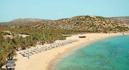 Hiekkaranta turkoosilla merellä, aurinkotuoleja ja varjoja. Tausta, jossa kasvillisuuden peittämiä vuoria. (Tekoälyn luoma teksti)