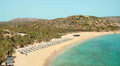 Hiekkaranta turkoosilla merellä, aurinkotuoleja ja varjoja. Tausta, jossa kasvillisuuden peittämiä vuoria. (Tekoälyn luoma teksti)