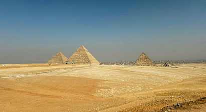 Kuvassa näkyvät Gizassa sijaitsevat suuret pyramidit ympäröityinä aavikkomaisemalla. (Tekoälyn luoma teksti)