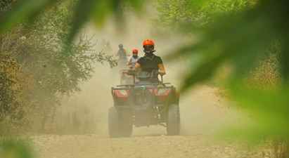 Henkilöt ajavat mönkijöillä pölyisellä soratiellä, jota ympäröi kasvillisuus. (Tekoälyn luoma teksti)