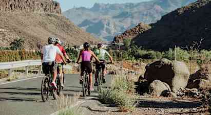Ryhmä pyöräilijöitä tiellä, jota ympäröivät kalliomäet ja vehreät laaksot. (Tekoälyn luoma teksti)