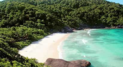 Kuva rannasta, jota ympäröivät vihreät vuoret ja sininen meri. (Tekoälyn luoma teksti)