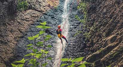 Henkilö laskeutuu köyden avulla vesiputouksen rinnettä, ympärillä kallioita ja kasvillisuutta. (Tekoälyn luoma teksti)
