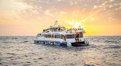 Lasipohjainen vene, jossa on ihmisiä, kulkee merellä auringonlaskun aikaan. (Tekoälyn luoma teksti)