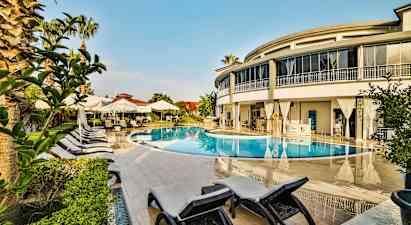 Ulkouima-allas, jota ympäröivät aurinkotuolit, aurinkovarjot ja moderni rakennus. (Tekoälyn luoma teksti)